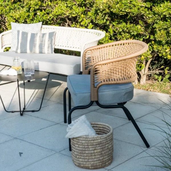 sillón de caño negro y cuerda beige con almohadón gris junto a una piscina. Hay una mesita lateral negra que sostiene una bandeja con refrescos