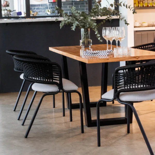 sillas de caño y cuerda negro con almohadón gris y una mesa de madera rectangular con paras de hierro en una sala