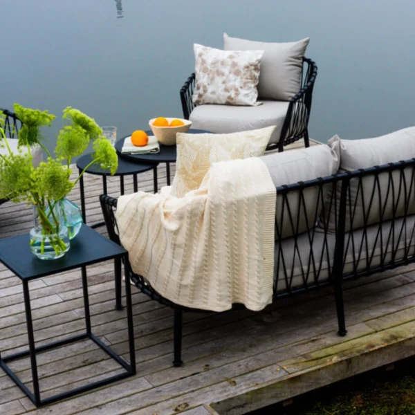 conjunto de sillones de cuerda y caño con mesa alta de lado sobre un deck de madera gastada junto a una laguna