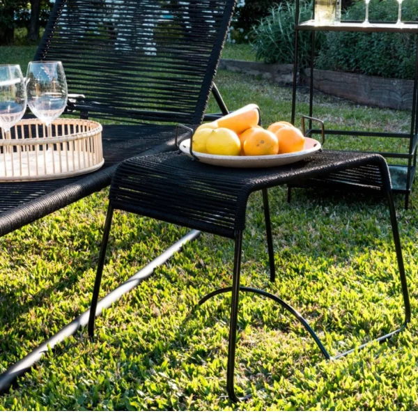 mesa de cuerda y caño negro en un jardín. Sobre la mesa hay un plato con naranjas