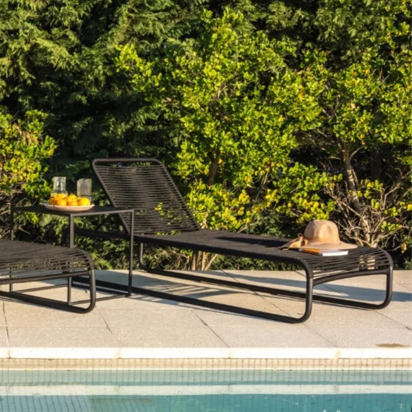 reposera de cuerda y caño negro junto a una mesa de chapa negra junto a una piscina. Sobre la mesa hay jugos de naranja