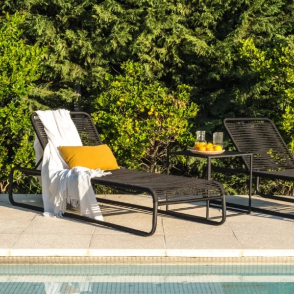 reposera de cuerda y caño negro junto a una mesa de chapa negra junto a una piscina