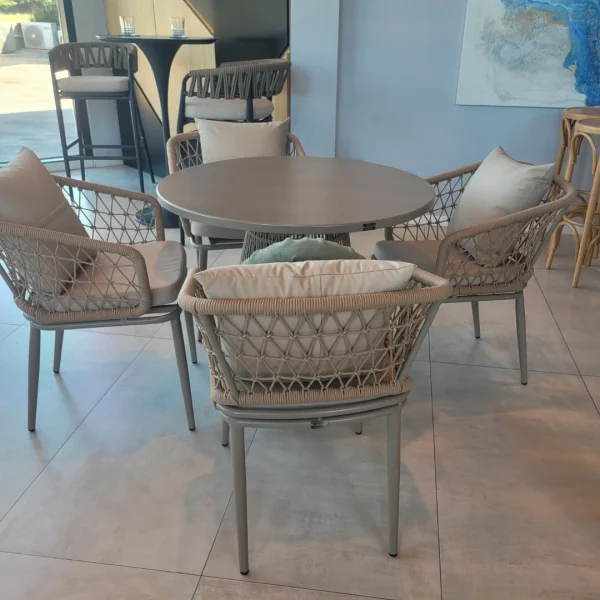 Conjunto de comedor TRAMA para exteriores con mesa redonda de aluminio y sillas de cuerda trenzada, en un ambiente moderno y acogedor.